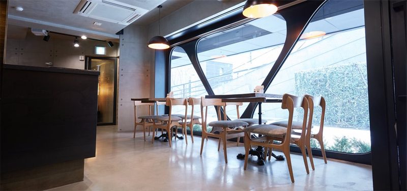 Hello K-POP Restaurant — 곡선 철골의 큰 통유리창 앞 원목 의자와 테이블, 펜던트 조명, 어두운 카운터